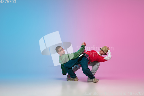 Image of Boys dancing hip-hop in stylish clothes on gradient background at dance hall in neon light.