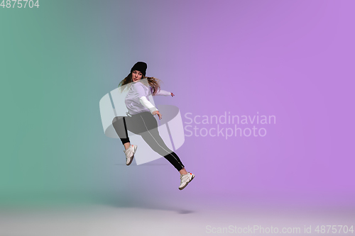Image of Girl dancing hip-hop in stylish clothes on gradient background at dance hall in neon light.