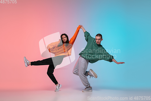 Image of Boy and girl dancing hip-hop in stylish clothes on gradient background at dance hall in neon light.