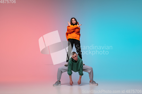 Image of Boy and girl dancing hip-hop in stylish clothes on gradient background at dance hall in neon light.