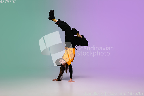 Image of Girl dancing hip-hop in stylish clothes on gradient background at dance hall in neon light.