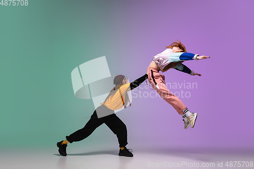 Image of Girls dancing hip-hop in stylish clothes on gradient background at dance hall in neon light.