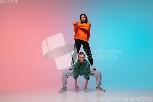 Image of Boy and girl dancing hip-hop in stylish clothes on gradient background at dance hall in neon light.