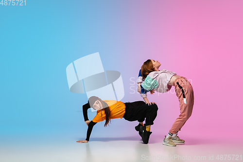 Image of Girls dancing hip-hop in stylish clothes on gradient background at dance hall in neon light.