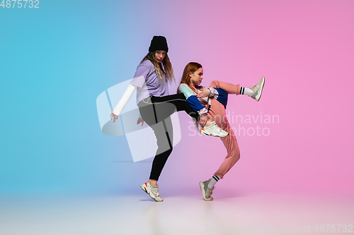 Image of Girls dancing hip-hop in stylish clothes on gradient background at dance hall in neon light.