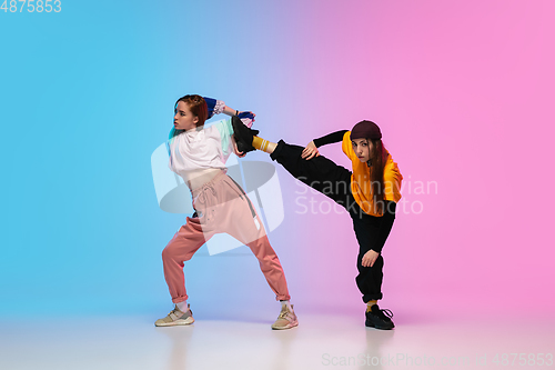 Image of Girls dancing hip-hop in stylish clothes on gradient background at dance hall in neon light.