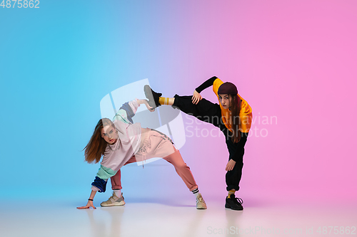 Image of Girls dancing hip-hop in stylish clothes on gradient background at dance hall in neon light.