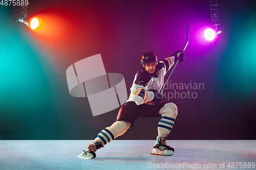 Image of Male hockey player with the stick on ice court and dark neon colored background