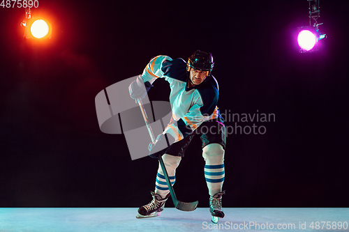 Image of Male hockey player with the stick on ice court and dark neon colored background