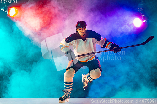 Image of Male hockey player with the stick on ice court and dark neon colored background