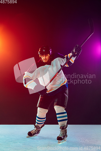 Image of Male hockey player with the stick on ice court and dark neon colored background