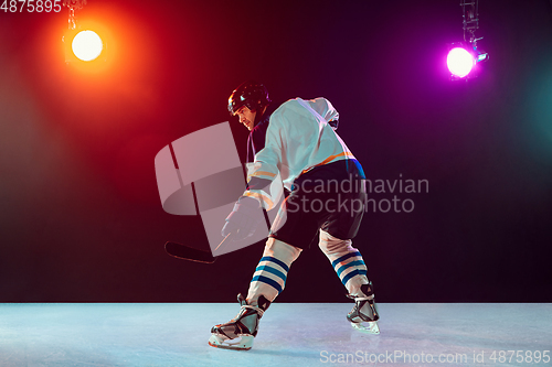 Image of Male hockey player with the stick on ice court and dark neon colored background