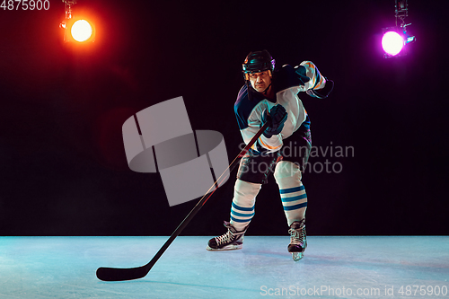 Image of Male hockey player with the stick on ice court and dark neon colored background