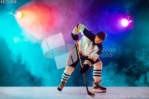 Image of Male hockey player with the stick on ice court and dark neon colored background