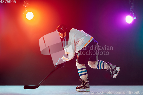 Image of Male hockey player with the stick on ice court and dark neon colored background