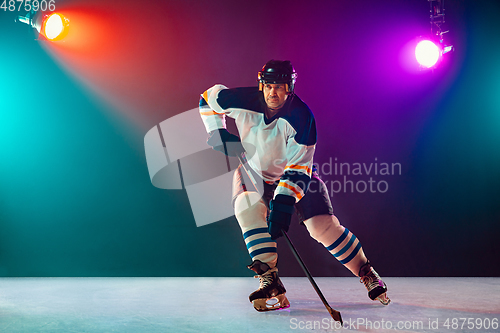 Image of Male hockey player with the stick on ice court and dark neon colored background