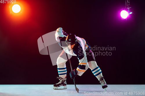 Image of Male hockey player with the stick on ice court and dark neon colored background