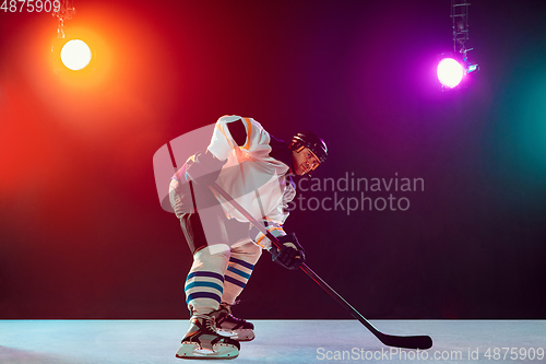 Image of Male hockey player with the stick on ice court and dark neon colored background