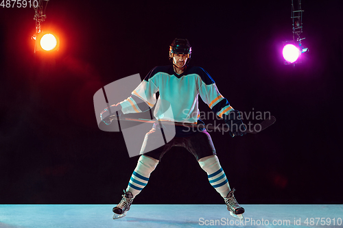 Image of Male hockey player with the stick on ice court and dark neon colored background