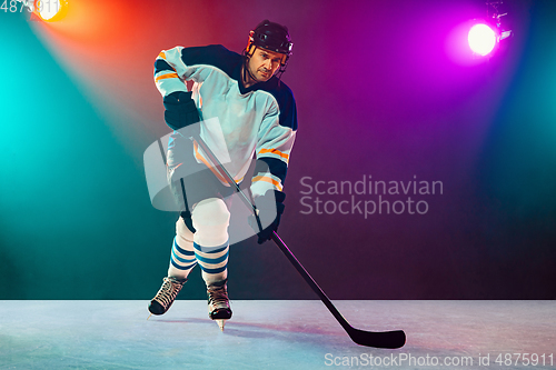 Image of Male hockey player with the stick on ice court and dark neon colored background