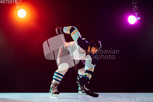 Image of Male hockey player with the stick on ice court and dark neon colored background