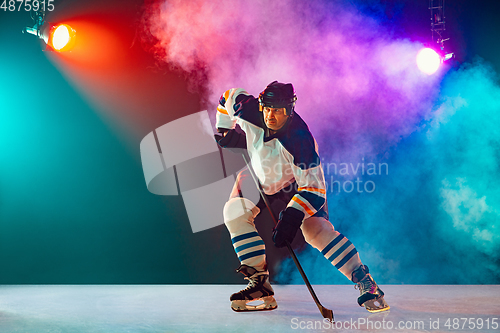 Image of Male hockey player with the stick on ice court and dark neon colored background