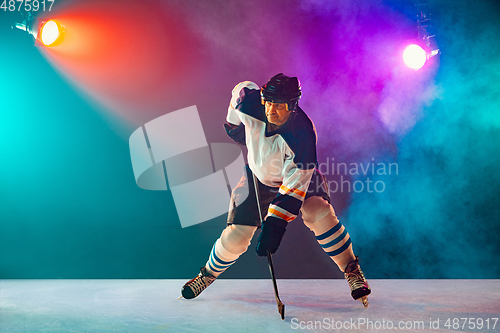 Image of Male hockey player with the stick on ice court and dark neon colored background