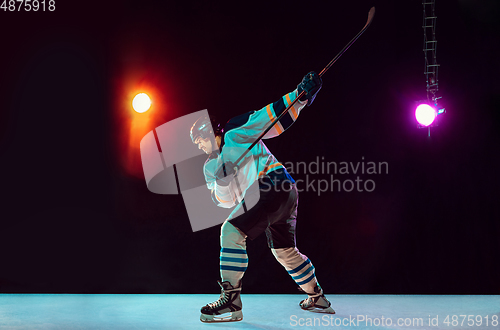 Image of Male hockey player with the stick on ice court and dark neon colored background