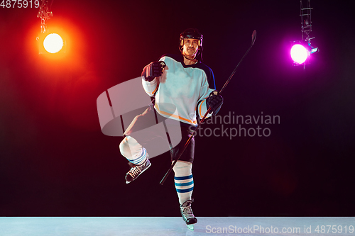 Image of Male hockey player with the stick on ice court and dark neon colored background