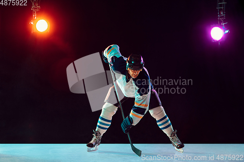 Image of Male hockey player with the stick on ice court and dark neon colored background