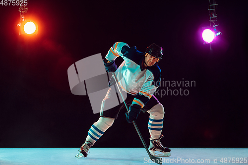 Image of Male hockey player with the stick on ice court and dark neon colored background