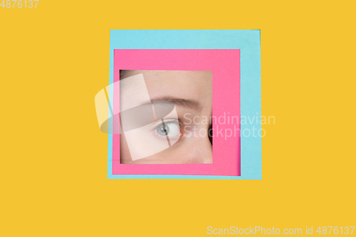 Image of Face of caucasian woman peeking throught square in yellow background