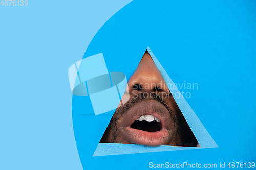 Image of Lips of african-american man peeking throught triangle in blue background