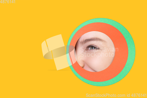 Image of Female eye peeking throught circle in yellow background