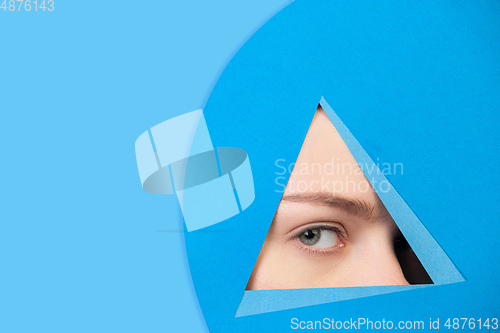 Image of Face of caucasian woman peeking throught triangle in blue background
