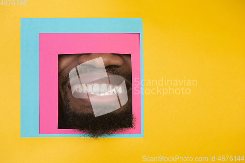 Image of Mouth of african-american man peeking throught square in yellow background