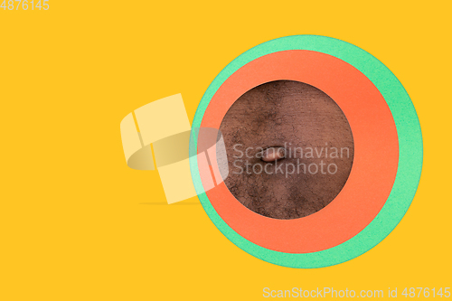 Image of Body of african-american man peeking throught circle in yellow background