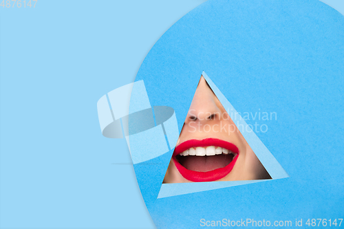 Image of Female red lips peeking throught triangle in blue background