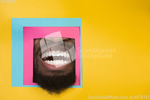 Image of Mouth of african-american man peeking throught square in yellow background