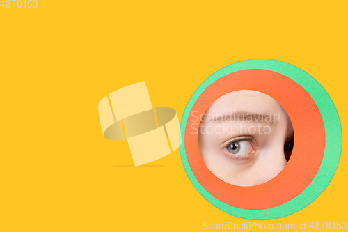 Image of Female eye peeking throught circle in yellow background