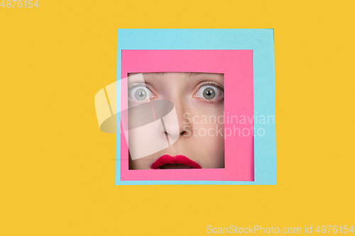 Image of Face of caucasian woman peeking throught square in yellow background