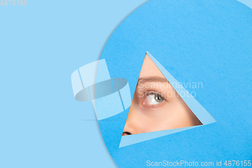 Image of Female eye looking, peeking throught triangle in blue background