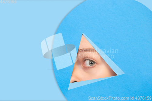 Image of Female eye looking, peeking throught triangle in blue background