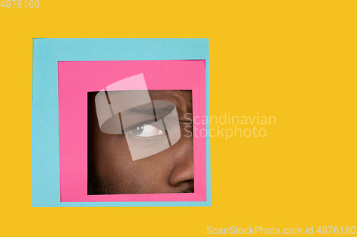 Image of Eye of african-american man peeking throught square in yellow background