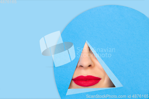 Image of Female red lips peeking throught triangle in blue background