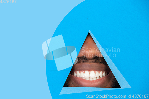 Image of Lips of african-american man peeking throught triangle in blue background