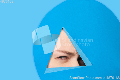 Image of Face of caucasian woman peeking throught triangle in blue background