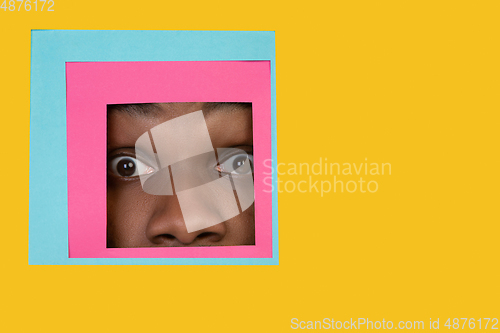 Image of Face of african-american man peeking throught square in yellow background