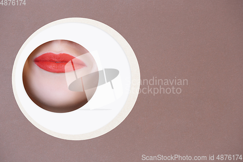 Image of Female face with red lips peeking throught circle in brown background