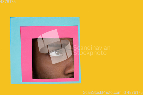 Image of Eye of african-american man peeking throught square in yellow background